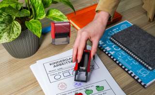 Kind zeigt stolz ein Arbeitsblatt mit Lehrer-Stempel im Klassenzimmer